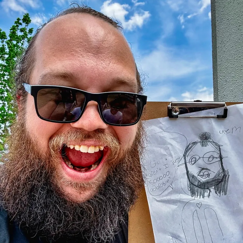 Andrew Hall smiling next to a student drawing of him at recess.